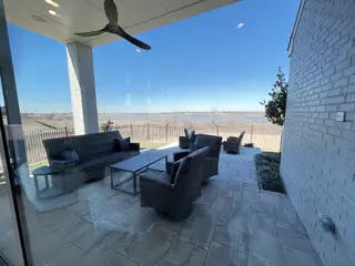 Model Home A sophisticated patio with wicker seating, ceiling fan, and scenic water views, perfect for relaxation.