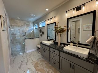 A luxurious bathroom with double sinks, dark granite countertop, sleek fixtures, and a spacious glass shower.