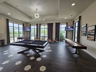 A chic game room with a modern pool table, shuffleboard, elegant lighting, and large windows for natural light.