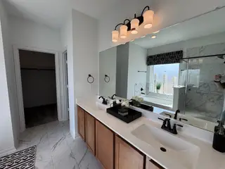 A modern bathroom with a dual-sink vanity, marble floor, glass shower, and elegant lighting.
