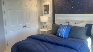 Model Home A cozy bedroom featuring a starry accent wall, blue bedding, and sleek modern decor.