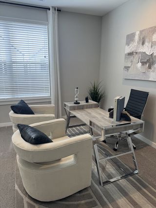 A modern office with chic white chairs, a sleek desk, abstract art, and ample natural light filtering through blinds.