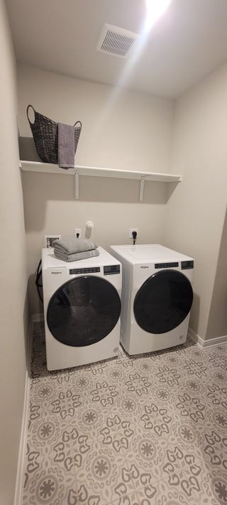 Model Home A modern laundry room featuring patterned tile flooring, a sleek washer and dryer, and convenient shelf storage above.