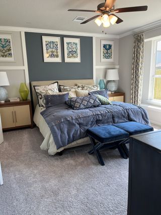 A cozy bedroom featuring a plush bed, textured blue accents, abstract art, and elegant furnishings under a warm ceiling fan.