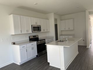 A bright, modern kitchen features white shaker cabinets, a stainless steel microwave and range, and a quartz countertop island with a sink.