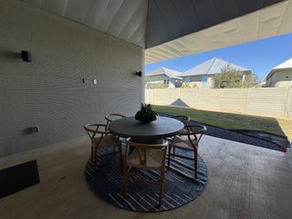 Model Home A modern patio with a sleek round table, wooden chairs, and a cozy blue rug overlooking a fenced backyard.