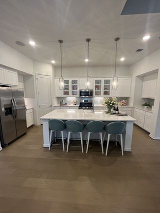 Model Home A bright, modern kitchen with white shaker cabinets, a large quartz island with seating, and warm wood flooring, illuminated by pendant lighting.