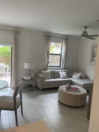 Model Home A cozy living room with a gray sectional, round ottoman, and soft natural light through large windows.