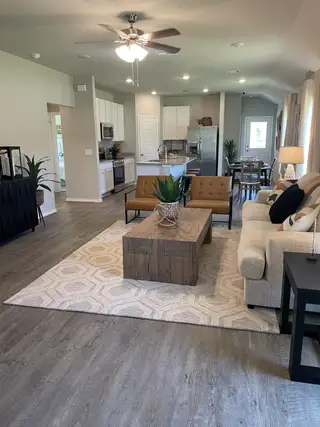Model Home A modern living area with wood flooring, a cozy sofa, and an open kitchen, featuring sleek cabinets and a dining area.