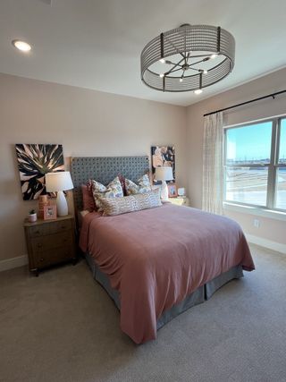 Model Home A cozy bedroom featuring a plush bed with soft pink bedding, elegant lighting, and a bright window view.