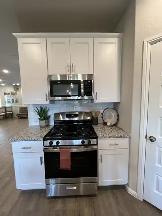 A modern kitchen with stainless steel appliances, white cabinetry, and granite countertops.