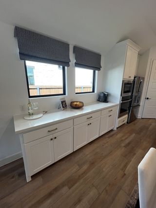 A modern kitchen with sleek white cabinets, wood flooring, and chic window treatments.