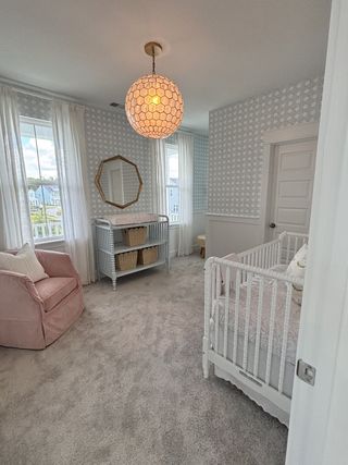 A cozy nursery with soft carpet, patterned wallpaper, and gentle lighting, featuring a crib and comfy armchair.