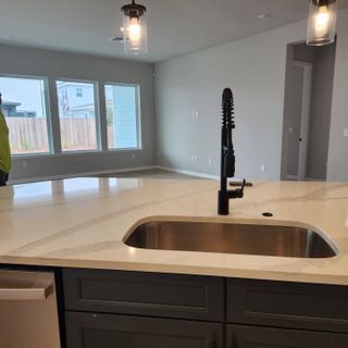 Modern kitchen with sleek gray cabinets, spacious marble island, and stylish pendant lighting. Large windows illuminate the space.