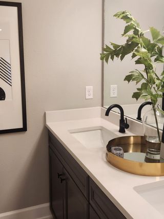 A modern bathroom with a sleek black faucet, decorative mirror, and elegant greenery in a glass vase.