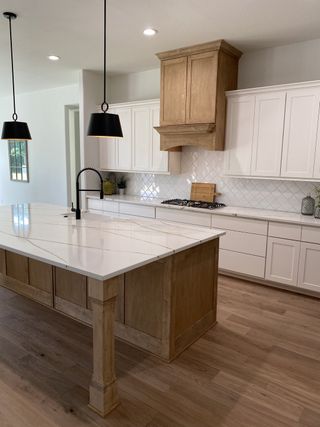 A modern kitchen with a sleek island, white cabinetry, and elegant pendant lighting over hardwood flooring.