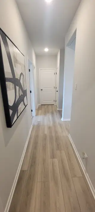Model Home A bright hallway featuring light wood flooring, white doors, and modern abstract artwork, creating an inviting atmosphere.
