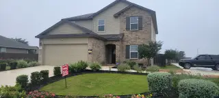 A two-story home in The Canyons at Amhurst by D.R. Horton (San Antonio, TX) with brick and siding, a two-car garage, and landscaped yard.