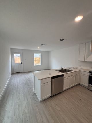 Model Home A modern kitchen with sleek white cabinets, an island, and stainless steel appliances open to a spacious living area.