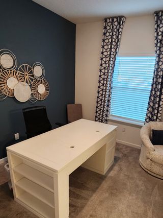 A cozy home office with a chic white desk, accent wall decor, and patterned curtains.