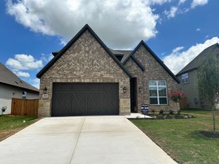 A charming brick home with a modern garage and landscaped yard in ShadowGlen by Terrata Homes (Manor, TX).