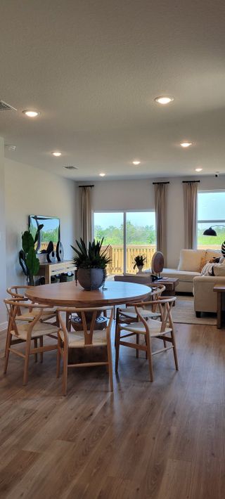A stylish dining space with a round wooden table, woven chairs, and large windows overlooking a private backyard.
