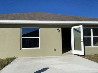 A modern beige facade with an open door and windows in Hickory Ridge by Adams Homes (Cocoa, FL).