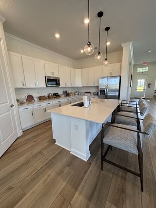 A modern kitchen with white cabinetry, a spacious island, pendant lighting, and elegant wood flooring.