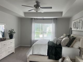 A cozy bedroom featuring a plush bed, elegant dresser, modern ceiling fan, and soothing neutral tones for a tranquil feel.