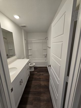 A sleek bathroom with a white vanity, dark flooring, and a shower-tub combo, offering a clean and contemporary feel. 