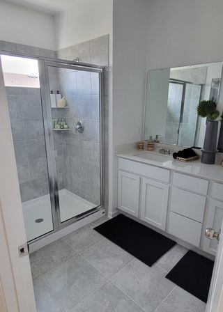 Model Home A sleek bathroom with a spacious glass shower, light gray tiles, and a white vanity, accented by modern decor.