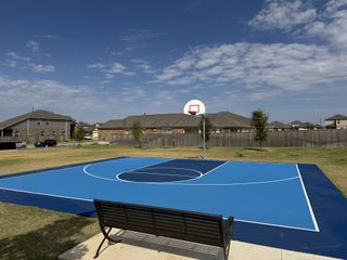 Community Amenities A vibrant blue basketball court with lush surroundings in Firefly Pointe: Cottage Collection by Lennar (Hutto, TX).