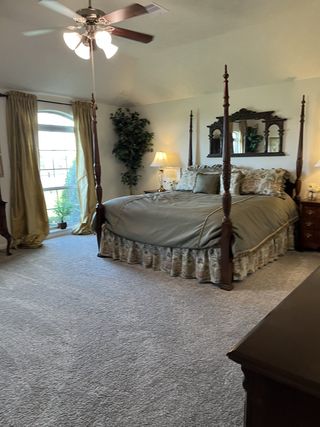 A cozy bedroom featuring a four-poster bed, elegant drapery, plush carpeting, and classic wooden furniture.