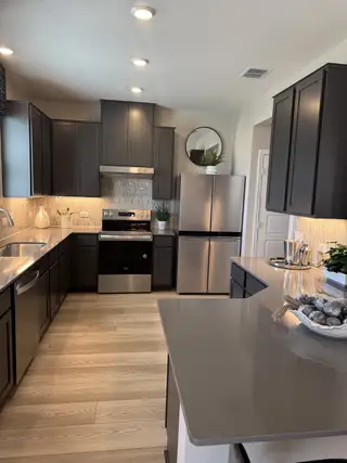 A modern kitchen featuring dark cabinetry, sleek stainless steel appliances, and elegant lighting on wood flooring.