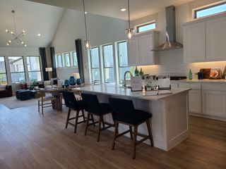 A modern kitchen and living space with high ceilings, large windows, and sleek lighting fixtures.