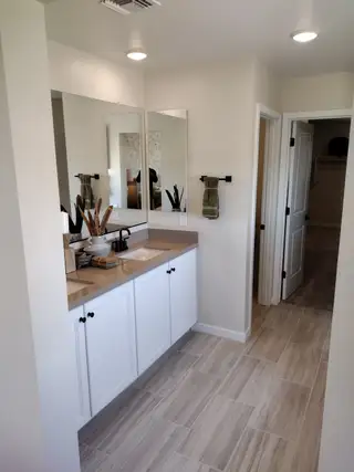 A modern bathroom with dual sinks, beige countertops, and sleek tile flooring.