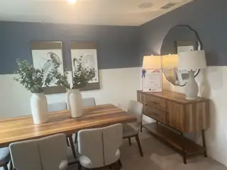 A modern dining area featuring a wooden table, gray chairs, abstract art, and elegant decor accents.