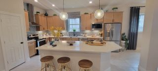 Model Home A modern kitchen featuring light wood cabinets, quartz countertops, and a stylish backsplash with pendant lighting over a large island.
