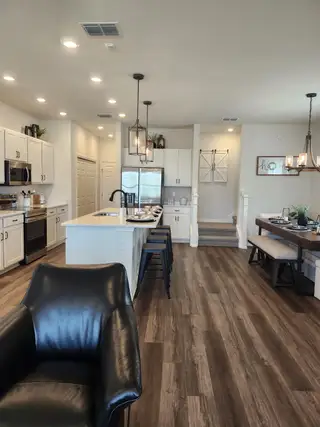 An open-concept kitchen with sleek white cabinets, island seating, and elegant pendant lighting over wood flooring.