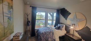 A cozy bedroom with aviation-themed decor, featuring a large window, camo bedding, and modern lighting.