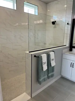 A sleek shower area with marble-style tiles, glass enclosure, and modern fixtures, accented by plush towels on a matte black rack.