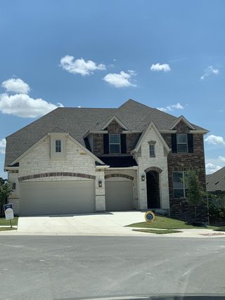 Street view A grand stone and brick home with a spacious three-car garage in Retreat at San Gabriel by Brightland Homes (Georgetown, TX).