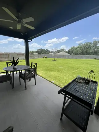 Model Home A covered patio with a ceiling fan overlooks a spacious, grassy backyard, perfect for outdoor dining and relaxation.
