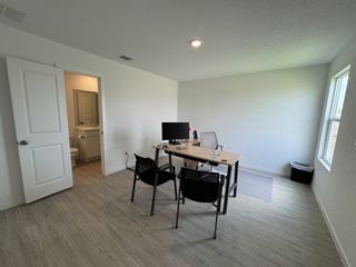 A bright home office with wood floors, a sleek desk, and window light. Adjoins an open bathroom for added convenience.