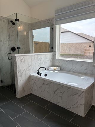 A modern bathroom with a marble-tiled shower, large window, deep bathtub, and sleek black fixtures.