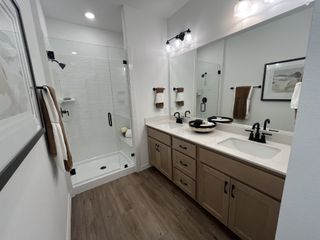 Model Home A modern bathroom featuring a dual vanity, glass-enclosed shower, and elegant wood flooring.