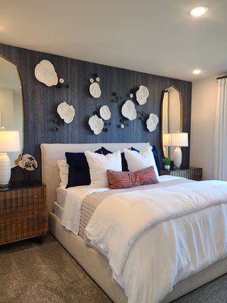 Model Home A cozy bedroom with a plush bed, textured accent wall, elegant mirrors, and modern decor, creating a serene retreat.