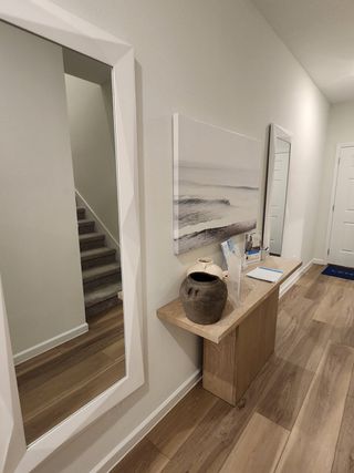 Model Home A modern hallway with wood flooring, a sleek console, coastal artwork, and mirrors alongside carpeted stairs.