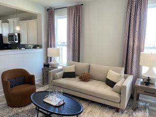 Model Home A cozy living room with a beige sofa, patterned curtains, modern lamps, and an open view to the kitchen.