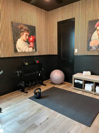 A stylish home gym with wood flooring, striped walls, workout equipment, and artistic decor.